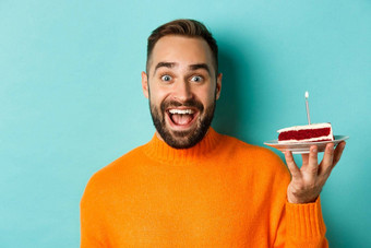 特写镜头快乐成人男人。庆祝生日持有bday蛋糕蜡烛使站绿松石背景