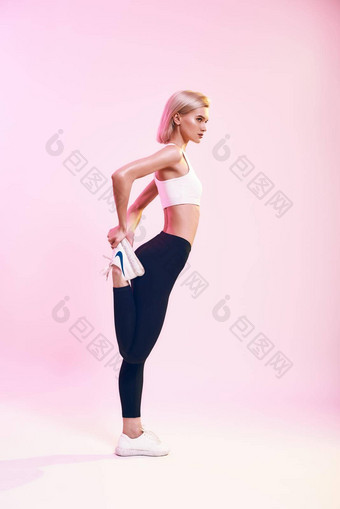强大的<strong>灵活</strong>的回来视图运动可爱的苗条的女人运动服装伸展运动腿站粉红色的背景工作室