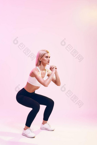 深蹲回来视图运动可爱的<strong>苗条</strong>的女人运动服装蹲站粉红色的背景工作室