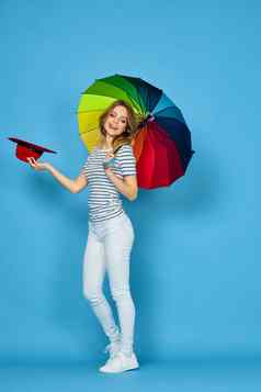 漂亮的女人时尚摆姿势色彩斑斓的伞蓝色的背景