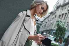 时尚年轻的时尚的女人站城市街应用程序智能手机集中特写镜头