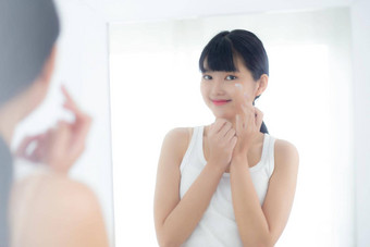 美丽的年轻的亚洲女人镜子应用保湿霜化妆品奶油乳液浴室<strong>首页护肤品</strong>卫生治疗身体护理皮肤抗衰老面部