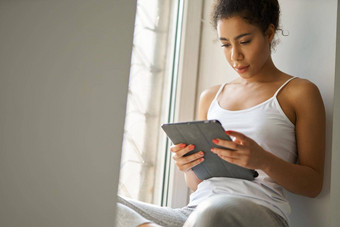 集中年轻的混合比赛女人阅读书平板电脑感觉舒适的坐着窗口首页