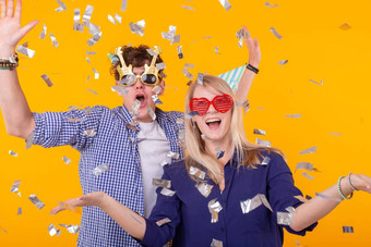 年轻的快乐的积极的夫妇有趣的眼镜纸帽喜乐喊黄色的背景飞行五彩纸屑概念假期有趣的