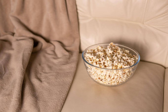 碗<strong>爆米花看电影</strong>米色沙发上零食不健康的垃圾食物概念
