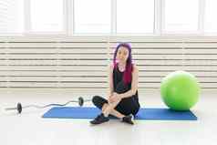 年轻的混合比赛女孩赶时髦的人紫色的头发坐着体育运动席杠铃健身球健身房概念常规的锻炼健身