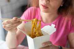 关闭手年轻的身份不明的女孩吃中国人面条木筷子坐着咖啡馆亚洲厨房概念