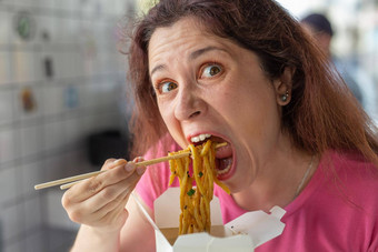 特写镜头肖像有趣的疯狂的年轻的漂亮的女孩吃中国人面条木筷子坐着咖啡馆概念饥饿饱腹感