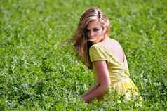 美丽的金发女郎女孩穿着绿色衣服坐着草地