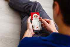 假期技术人概念男人。服装圣诞老人老人智能手机礼物圣诞节树坐着扶手椅灯背景