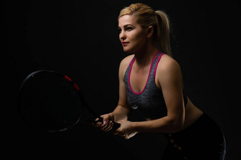 年轻的女网球球员摆姿势球拍黑色的背景