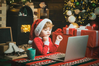 圣诞节孩子男孩电脑移动PC首页圣诞节背景孩子穿圣诞老人衣服坐着移动PC圣诞老人助手笔记本