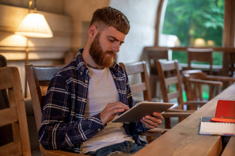 自由职业者穿着休闲装焦点阅读新闻数字平板电脑坐着舒适的城市咖啡馆