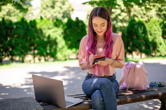 女人写作笔记本坐着木板凳上公园女孩工作在户外可移植的电脑复制空间