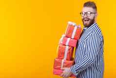惊讶年轻的赶时髦的人的家伙眼镜持有大堆栈礼物盒子黄色的背景复制空间概念一年圣诞节礼物