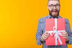 快乐的年轻的赶时髦的人的家伙胡子眼镜拥抱红色的礼物盒子黄色的背景复制空间概念快乐礼物