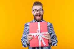 快乐的年轻的赶时髦的人的家伙胡子眼镜拥抱红色的礼物盒子黄色的背景概念快乐礼物