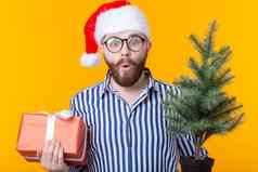 积极的年轻的男人。圣诞老人老人礼物圣诞节树摆姿势黄色的背景圣诞节一年假期概念