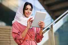 年轻的阿拉伯女人穿戴数字平板电脑在户外