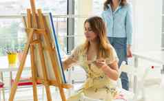 艺术学校创造力休闲概念学生女孩年轻的女人艺术家画架调色板油漆刷绘画图片工作室老师帮助