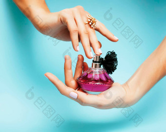 女人手持有瓶香水粉红色的修指甲珠宝蓝色的背景奢侈品概念