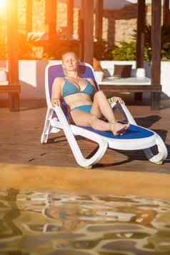 年轻的女人放松甲板椅子游泳池度假胜地太阳耀斑