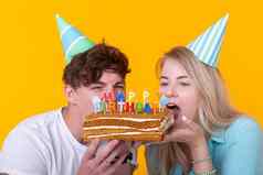关闭奇怪的年轻的夫妇女孩男孩纸帽子咬一块祝贺的蛋糕生日祝贺你概念