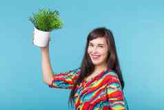快乐的年轻的女人持有能植物摆姿势蓝色的背景概念园艺室内配件