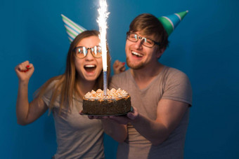 有趣的年轻的夫妇纸帽蛋糕使愚蠢的脸快乐生日站蓝色的背景概念祝贺你愚弄