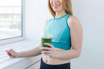 健康的健身排毒概念关闭年轻的女人体育穿绿色奶昔微笑在室内