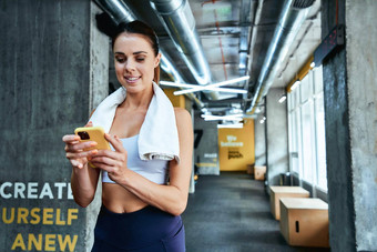 聊天朋友年轻的集中健身女人运动服装智能手机发短信短信站健身房休息锻炼