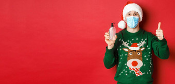 概念一年冠状病毒社会距离肖像快乐的男人。圣诞老人他圣诞节毛衣医疗面具显示翘拇指推荐手洗手液