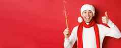 概念圣诞节冬天假期庆祝活动英俊的男人。庆祝一年有趣的持有炯炯有神的眼睛显示翘拇指站红色的背景