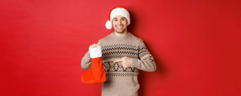 概念冬天假期一年庆祝活动英俊的微笑男人。准备礼物孩子们指出圣诞节长袜袋站红色的背景