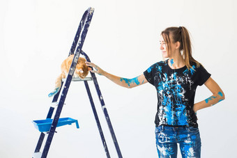 年轻的女人画家抚摸猫设计师工人油漆墙宠物坐在梯工作