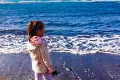 女孩穿夹克玩海滩海洋多云的天空冬天时间