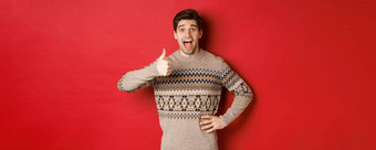 肖像兴奋有吸引力的男人。圣诞节毛衣显示竖起大拇指惊讶推荐好事情广告圣诞节相关的产品