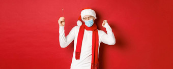 概念科维德圣诞节假期流感大流行快乐男人。庆祝一年聚会，派对穿医疗面具圣诞老人他跳舞炯炯有神的眼睛红色的背景