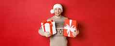 图像快乐的有吸引力的的家伙持有圣诞节礼物站圣诞老人他冬天毛衣微笑快乐站红色的背景