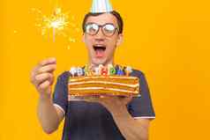 疯狂的快乐的年轻的男人。眼镜纸祝贺的帽子持有蛋糕快乐生日站黄色的背景禧年祝贺你概念