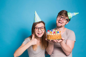 有趣的年轻的夫妇纸帽蛋糕使愚蠢的脸快乐生日站蓝色的背景概念祝贺你愚弄