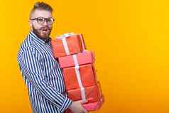 惊讶年轻的赶时髦的人的家伙眼镜持有大堆栈礼物盒子黄色的背景复制空间概念一年圣诞节礼物