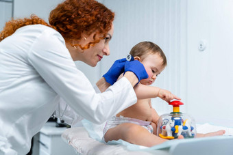红发女医生检查孩子一年现代诊所儿科医生检查婴儿医院儿童医疗保健诊断治疗孩子