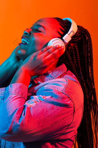 非洲美国年轻的女人听音乐在线跳舞唱歌耳机霓虹灯光音乐技术概念