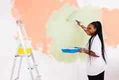 年轻的快乐非洲美国女人绘画室内墙油漆辊房子女人辊应用油漆墙