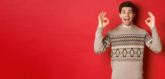 概念圣诞节庆祝活动冬天假期生活方式肖像英俊的男人。毛衣惊讶显示迹象保证推荐好红色的背景