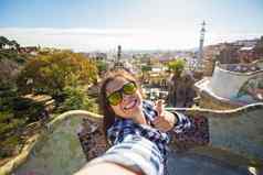 旅行假期概念美丽的年轻的女人相机采取照片聪明的电话微笑公园平息我巴塞罗那西班牙