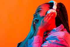 年轻的非裔美国人女人听音乐耳机霓虹灯光女肖像概念人类情绪面部表达式假期周末爱好