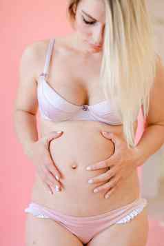 年轻的怀孕了女人持有肚子粉红色的单声道的背景