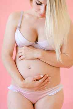 年轻的怀孕了女人持有肚子粉红色的单声道的背景